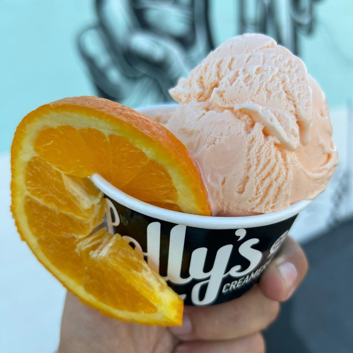 Hand holding Lolly's ice cream cup with ice cream and orange slice.