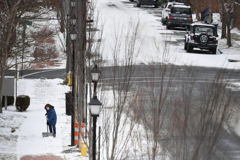 Photo of a woman shovels a sidewalk along Bernard St. after a storm hit the area in Virginia.